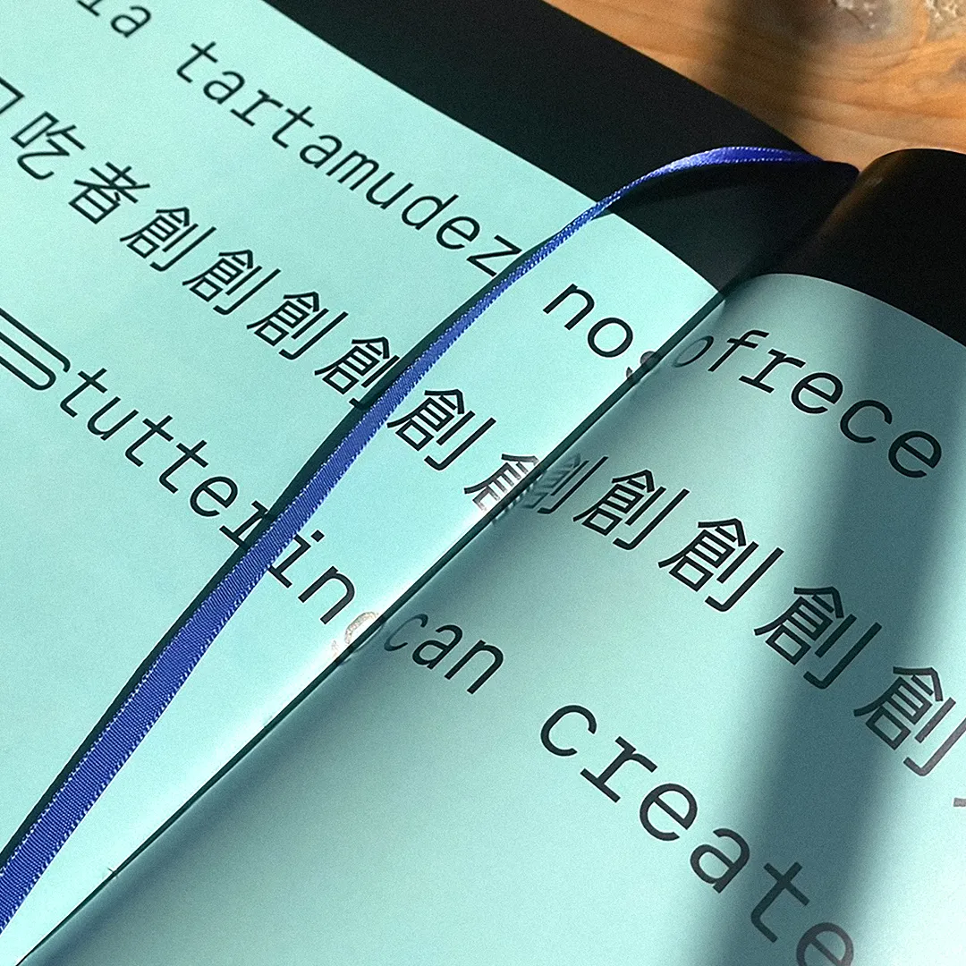 A close up of a book, with the design of the billboard by People Who Stutter Create. It is green-blue with black typography.