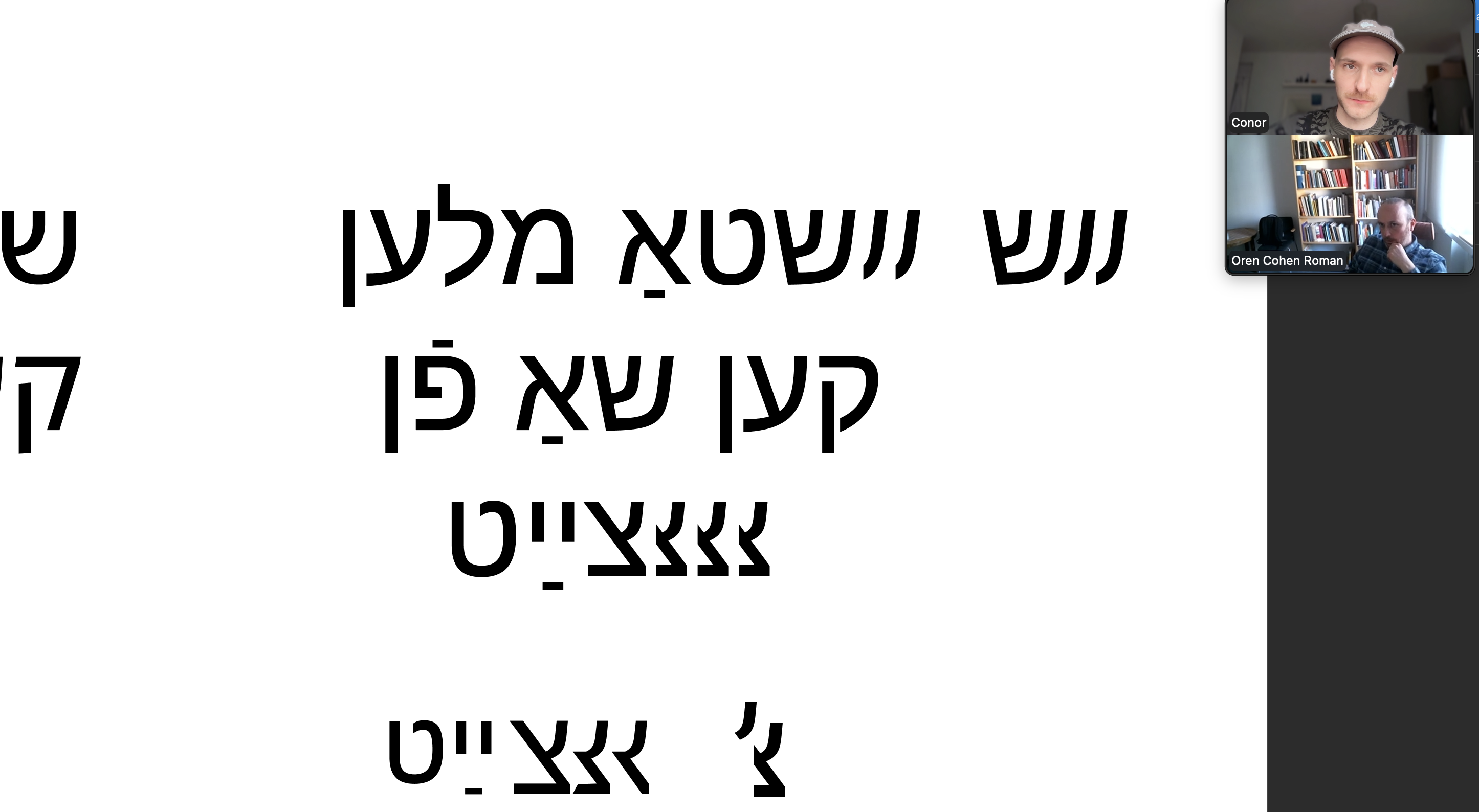 Screenshot of a video call between two men. In the centre of the frame is a white digital canvas with black typography in Yiddish.